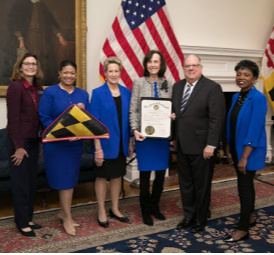 Maryland Governor Larry Hogan, State Superintendent of Schools Dr. Karen B. Salmon with 4 representatives from Pinewood Elementary School holding a certificate and a Maryland flag.