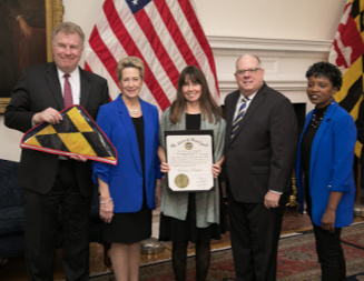 Maryland Governor Larry Hogan, State Superintendent of Schools Dr. Karen B. Salmon with 2 representatives from Ocean City Elementary School holding a certificate and a Maryland flag.