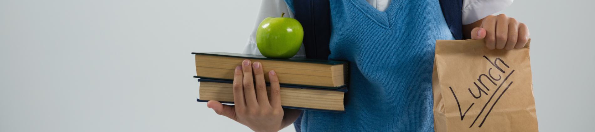 A child holding a paper bagged lunch and a stack of books.